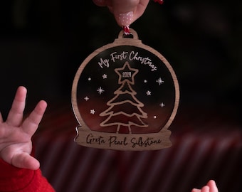 May include: A wooden globe-shaped Christmas ornament featuring a dark gradient background, a central engraved Christmas tree with a star topper labeled 2024, and the text My First Christmas and Greta Pearl Silkstone.