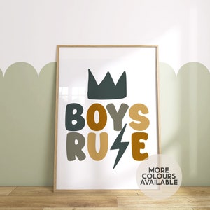 May include: A framed print with the text "BOYS RULE" in a stylised font. The letters are in shades of brown, green, and yellow. A crown is above the text. The print has a white background and a wooden frame.