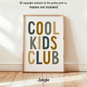 May include: A rectangular wall art print featuring the text COOL KIDS CLUB in a bold, sans-serif font. The letters are colored in alternating shades of dark green, mustard yellow, and olive green against a plain white background.