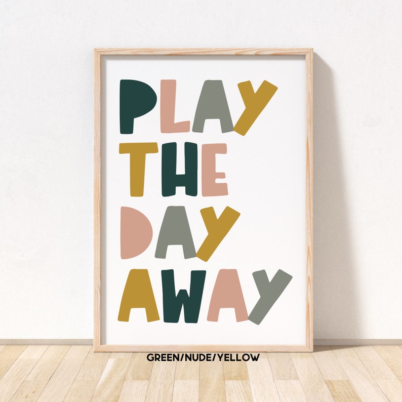 May include: A framed print with the text "PLAY THE DAY AWAY" in colorful, stylized letters. The letters are in shades of green, nude, and yellow.