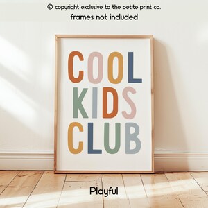 May include: A rectangular wall art print featuring the text COOL KIDS CLUB in a bold, sans-serif font. The letters are colored in muted shades of orange, pink, yellow, blue, and sage green against a white background. The print is displayed in a frame.