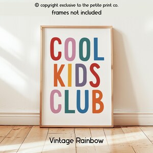 May include: A rectangular wall art print featuring the text COOL KIDS CLUB in large, multi-colored sans-serif letters. The letters are colored in red, pink, teal, blue, orange, and purple. The print is displayed in a light wood frame.