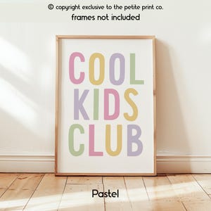 May include: A rectangular wall art print featuring the text COOL KIDS CLUB in large, sans-serif capital letters. The letters are colored in alternating pastel shades of pink, yellow, purple, and green against a plain white background.