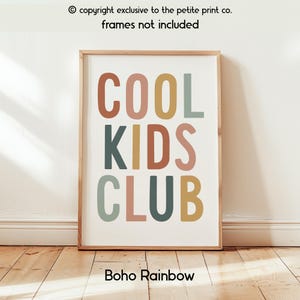 May include: A rectangular wall art print featuring the text COOL KIDS CLUB in a stacked, sans-serif font. The letters are colored in muted shades of terracotta, mustard yellow, and sage green against a plain off-white background.