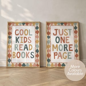 May include: Two rectangular wall art prints in light wood frames. The left print features the text COOL KIDS READ BOOKS, and the right print features the text JUST ONE MORE PAGE. Both have a border of colourful diamonds in muted tones.