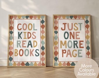 May include: Two rectangular wall art prints in light wood frames. The left print features the text COOL KIDS READ BOOKS, and the right print features the text JUST ONE MORE PAGE. Both have a border of colourful diamonds in muted tones.