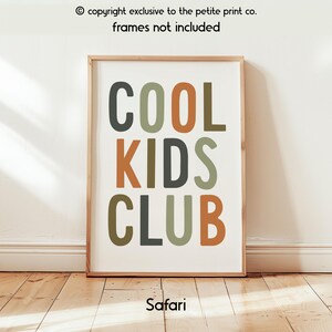May include: A rectangular wall art print featuring the text COOL KIDS CLUB in a stacked, sans-serif font. The letters are colored in shades of dark gray, muted green, and burnt orange. The text copyright exclusive to the petite print co. frames not included is visible at the top, and the word Safari is at the bottom.