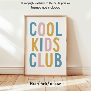 May include: A rectangular wall art print featuring the text COOL KIDS CLUB in a bold, sans-serif font. The letters are colored in alternating shades of muted blue, soft pink, and mustard yellow against a plain white background.