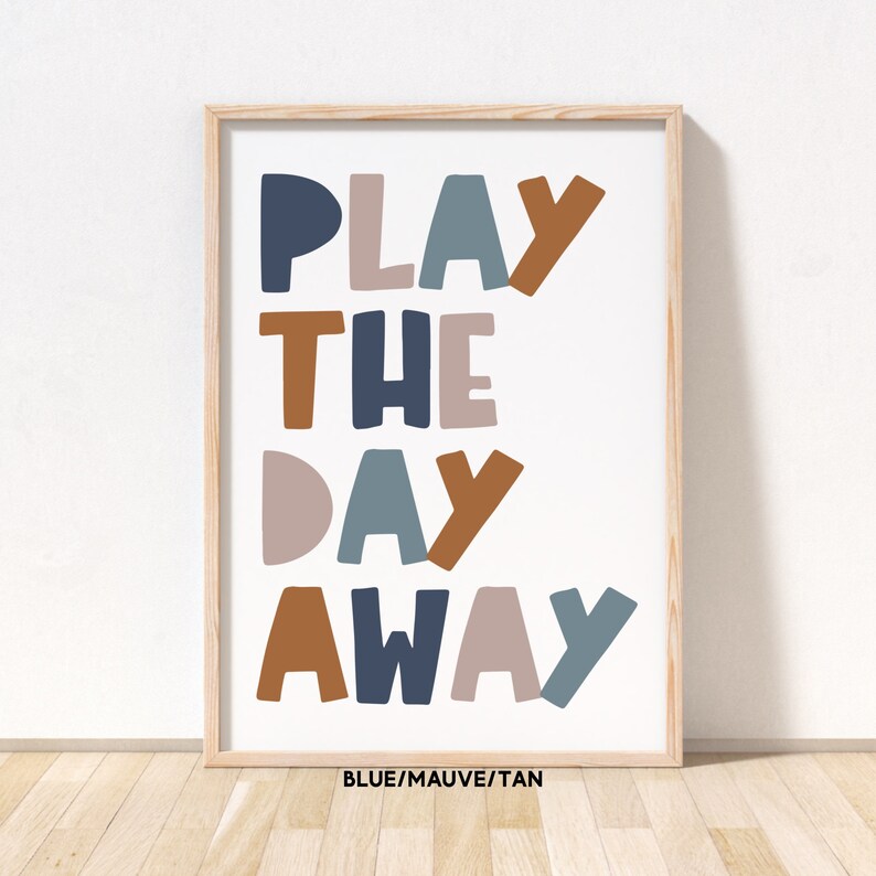 May include: A framed print with the text "PLAY THE DAY AWAY" in blue, mauve, and tan colors. The text is in a playful, oversized font.