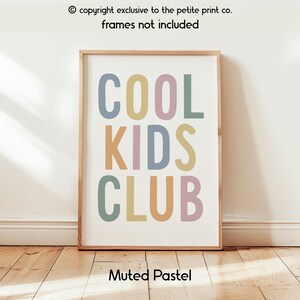 May include: A rectangular wall art print featuring the text COOL KIDS CLUB in large, sans-serif capital letters. Each letter is colored in a different muted pastel shade, including dusty blue, soft yellow, muted pink, and sage green on a white background.