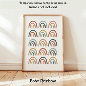 Op de afbeelding: Een ingelijste print met een herhalend patroon van regenboogbogen in bruine, groene en gele tinten. De tekst "Boho Rainbow" staat onderaan. De tekst "copyright exclusive to the petite print co. frames not included" staat bovenaan.