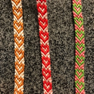 May include: Three friendship bracelets with chevron patterns in orange and white, red and white, and green and pink.
