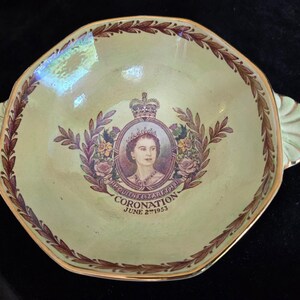 Op de afbeelding: Een vintage, lichtgroene, achthoekige schaal met gouden randen en handvatten. Het midden toont een portret van koningin Elizabeth II, omringd door een bloemenkrans en de tekst "CORONATION JUNE 2nd 1953".