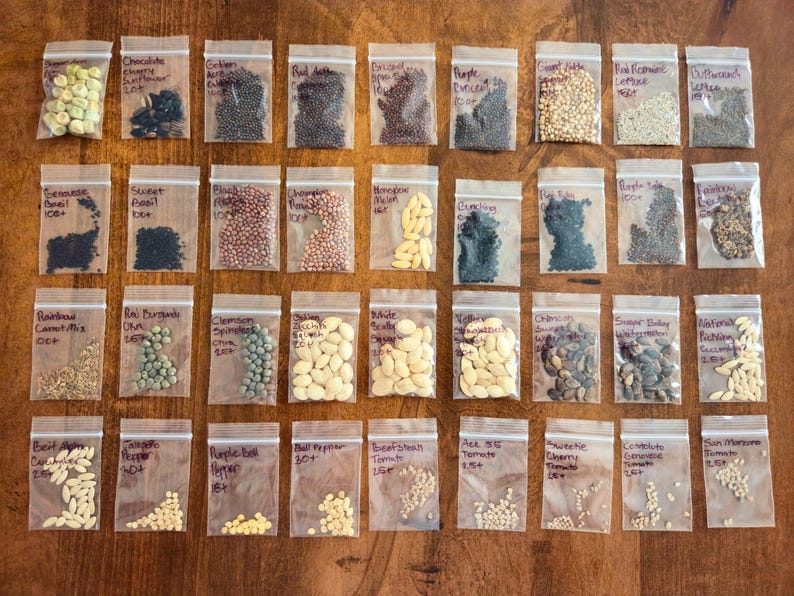 May include: A collection of seed packets, each labeled with the variety of seeds inside. The packets are arranged on a wooden surface. Varieties include basil, tomatoes, and peppers. The image is a top-down view.