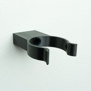 May include: A black plastic wall mount hook with a single hole for hanging items.