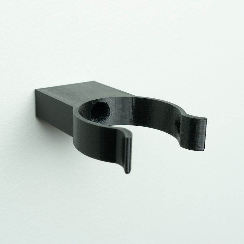 May include: A black plastic wall mount hook with a single hole for hanging items.