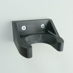 May include: A black plastic wall mount with a curved hook for hanging items. The mount has two silver screws.