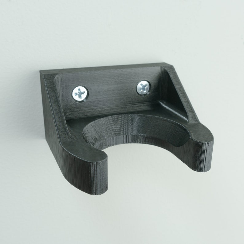 May include: A black plastic wall mount with a curved hook for hanging items. The mount has two silver screws.