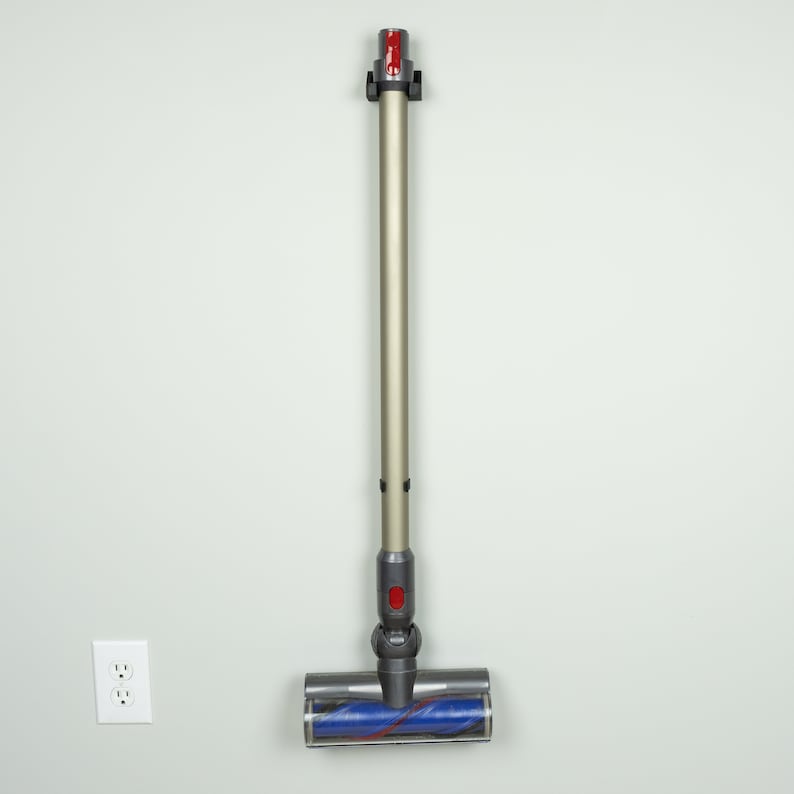 May include: A gray and silver handheld vacuum cleaner with a blue and red roller brush head is mounted on a white wall.