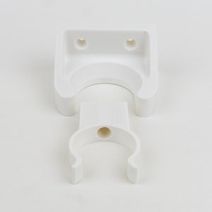 May include: White plastic wall mount with a U-shaped hook. The mount has two holes for screws.