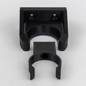 May include: Black plastic wall mount with a circular opening for hanging items. The mount is in two pieces, a base and a hook.