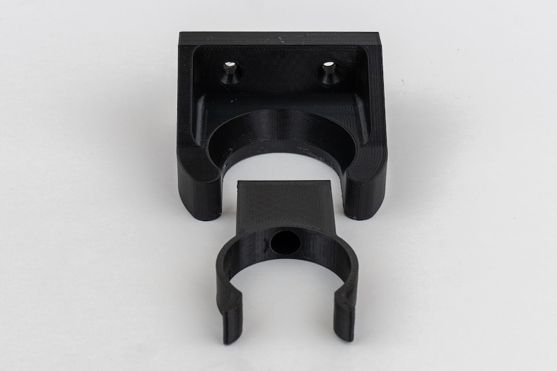 May include: Black plastic wall mount with a circular opening for hanging items. The mount is in two pieces, a base and a hook.