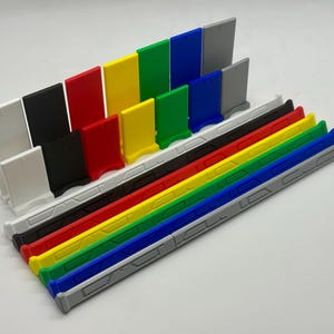 May include: A set of colorful plastic dividers with a white base. The dividers are arranged in a row, with the tallest divider on the left and the shortest divider on the right. The dividers are all different colors, including red, yellow, green, blue, and black.