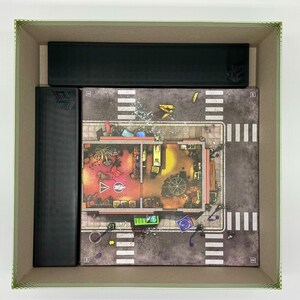 May include: A game board with a city street scene and a building with a red and yellow interior. The board is surrounded by black cardboard boxes.