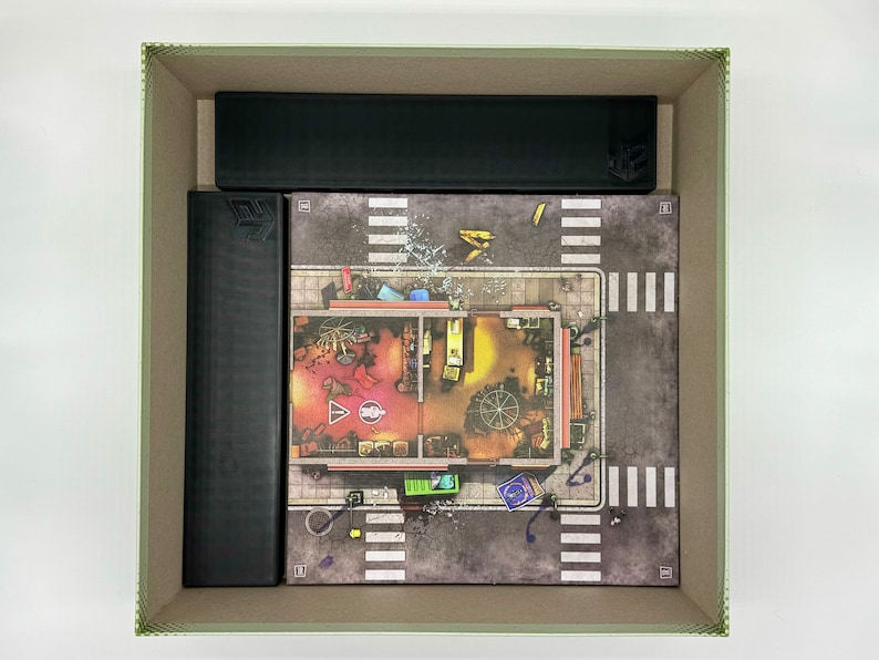 May include: A game board with a city street scene and a building with a red and yellow interior. The board is surrounded by black cardboard boxes.