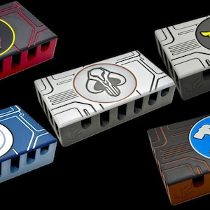 Op de afbeelding: Vijf rechthoekige, veelkleurige dozen met diverse cirkelvormige emblemen. De dozen hebben een printplaatontwerp en een reeks sleuven. De emblemen zijn rood, geel, wit en blauw, met diverse grafische ontwerpen.
