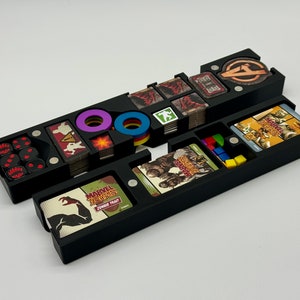 May include: Black plastic organizer with compartments for storing game pieces and cards. The organizer has a compartment for dice, tokens, and cards. The organizer is labeled "Marvel Zombies:  Zombie Trait".