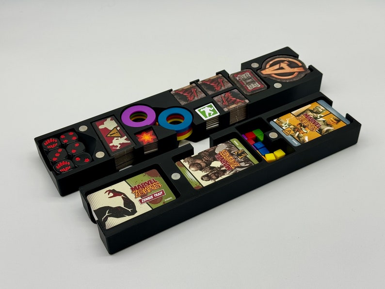 May include: Black plastic organizer with compartments for storing game pieces and cards. The organizer has a compartment for dice, tokens, and cards. The organizer is labeled "Marvel Zombies:  Zombie Trait".