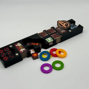 May include: Black plastic organizer with compartments for dice, tokens, and cards. The organizer has a compartment for dice, a compartment for tokens, and a compartment for cards. There are also several compartments for smaller items. The organizer is filled with various game pieces, including dice, tokens, and cards.