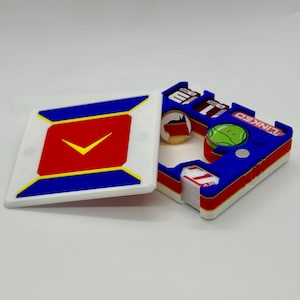 Op de afbeelding: Een set kleurrijke, geometrische spelstukken. Eén stuk is een witte vierkant met een rood en geel ontwerp en een vinkje. Het andere stuk is blauw, rood en wit met het woord "LINKED" erop.