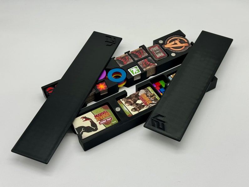 May include: Black organizer with multiple compartments for storing game pieces and cards. The organizer has a lid that opens to reveal the compartments. The compartments are labeled with the names of the game pieces and cards. The organizer is made of plastic and has a smooth finish.