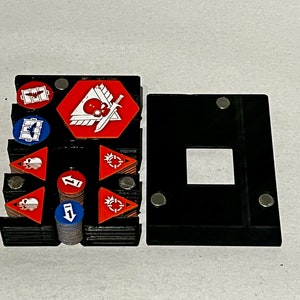 May include: A black plastic storage box with a magnetic closure. The box is filled with small, colorful, round and triangular tokens with white designs. The box is designed to hold and organize game pieces.