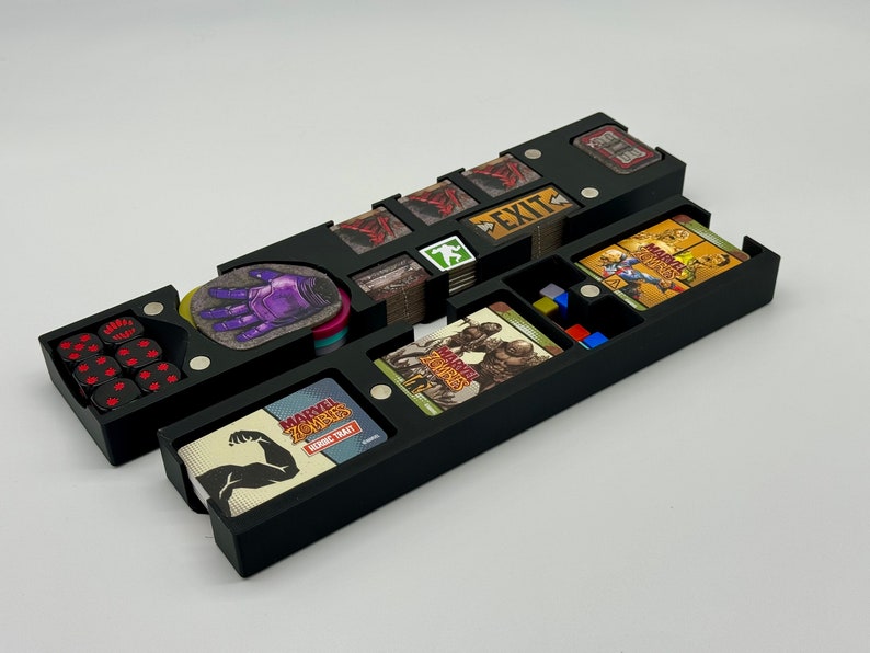 May include: Black plastic organizer with compartments for storing a board game. The organizer has a compartment for dice, a compartment for cards, and a compartment for tokens. The organizer is labeled "Marvel Zombies:  Heroic Trait".