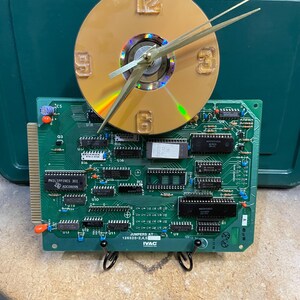 May include: A unique clock made from a repurposed CD and a green circuit board. The clock face is a gold-colored CD with gold-colored hands and raised numerals. The circuit board has various electronic components and the text "PHILIPPINES 301" and "JUMPERS AT 126525-2,4,5 IVAC".