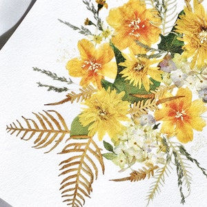 Pu&ograve; includere: Primo piano di una composizione di fiori pressati con fiori gialli e arancioni, foglie verdi e fronde di felce secche. I fiori sono disposti su uno sfondo bianco, creando un'estetica delicata e naturale. La composizione &egrave; ben illuminata.