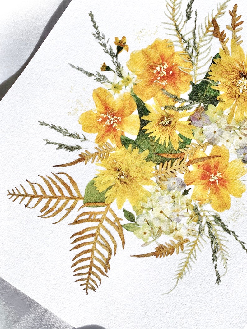 Pu&ograve; includere: Primo piano di una composizione di fiori pressati con fiori gialli e arancioni, foglie verdi e fronde di felce secche. I fiori sono disposti su uno sfondo bianco, creando un'estetica delicata e naturale. La composizione &egrave; ben illuminata.