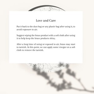 May include: A white card with the text "Love and Care" and instructions for brass product maintenance. The card is set against a neutral background with a marble-like texture and a plant shadow.
