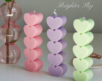 May include: Three stacked heart-shaped candles in pink, purple, and green. The candles are arranged in a row on a white surface. The text "Brighter Sky" is visible in the top right corner of the image.