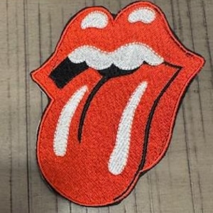 May include: Embroidered patch of the Rolling Stones' tongue and lips logo. The patch has a red background with white and black detailing, and a black border. It's designed for application on clothing or accessories.
