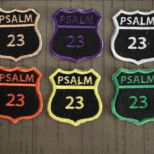 May include: Six embroidered patches in a road sign shape, each with the word "PSALM" above the number "23". The patches have black backgrounds with borders in tan, purple, white, orange, yellow, and green.