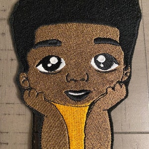 Pode incluir: Patch bordado de uma criança de pele morena com cabelo preto, vestindo uma camisa amarela e olhando para cima com um sorriso.