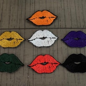 以下が含まれることがあります： オレンジ、黄色、白、紫、緑、赤、黒の様々な色の刺繍された唇のパッチ。これらのパッチは、衣類、バッグ、アクセサリーにユニークなタッチを加えるのに最適です。パッチは木製の表面に配置されています。