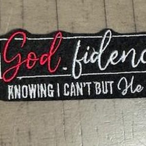 May include: A black rectangular patch with white and red embroidered text. The patch reads "God.fidence" in a cursive font, with the words "KNOWING I CAN'T BUT He CAN" below in a sans-serif font.
