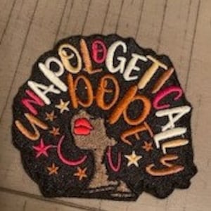 Op de afbeelding: Gestikt patch met een zwart silhouet van een vrouwenhoofd met een afro-kapsel. De tekst "Unapologetically Dope" is in een cirkel rond het silhouet geschreven. Het patch heeft een zwarte achtergrond met gouden, witte en roze accenten.