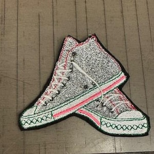 May include: A pair of silver glitter high-top sneakers with pink and green trim. The sneakers are embroidered with white laces.