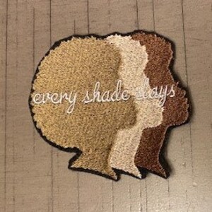 Pode incluir: Etiqueta bordada com três silhuetas de rostos de mulheres em tons de marrom, bege e branco. O texto "every shade says" é bordado em branco abaixo das silhuetas.